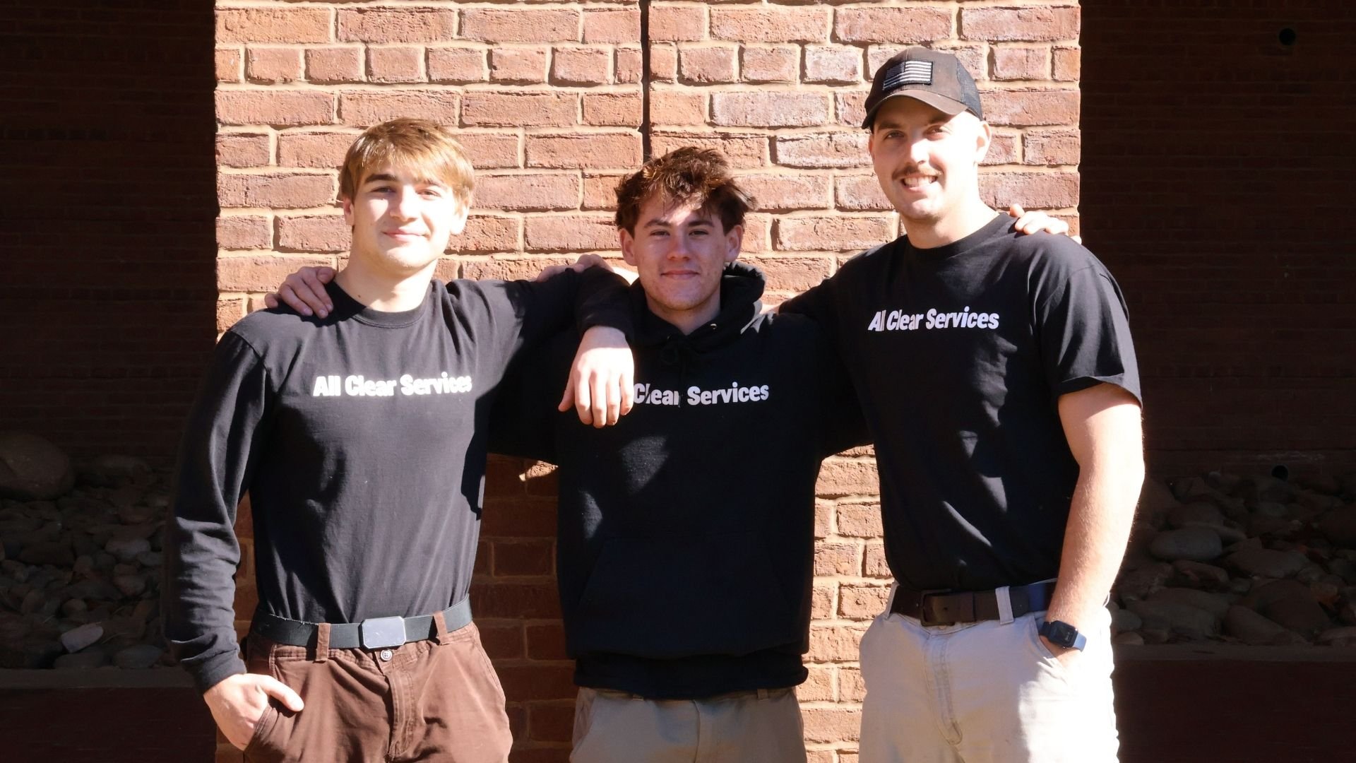 Moving company employees standing together in matching black shirts against brick wall